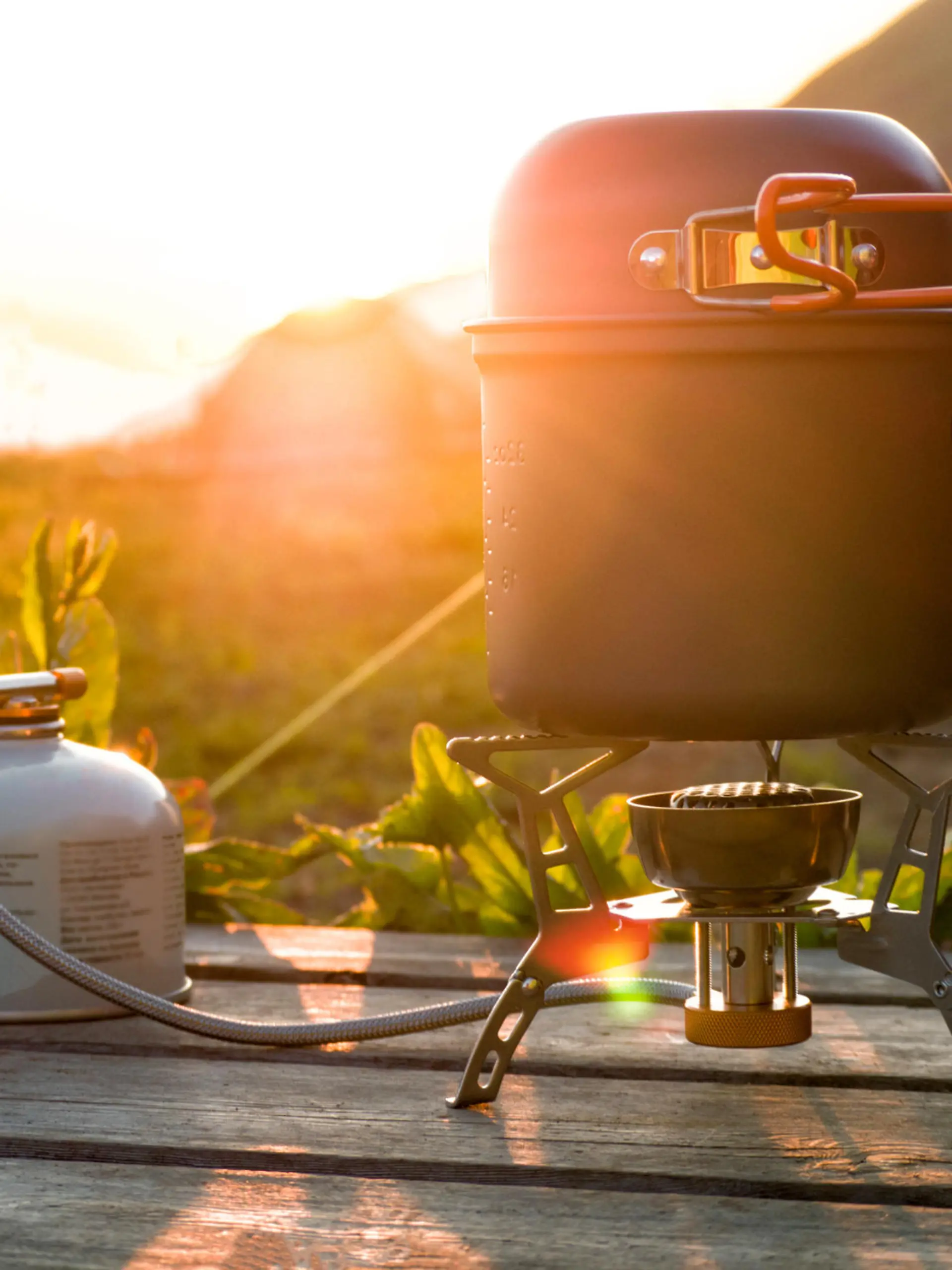 Cooking pot on camping gas stove and canister on wooden table at sunlight background. Travel equipment for hiking and backpacking at beautiful sunset