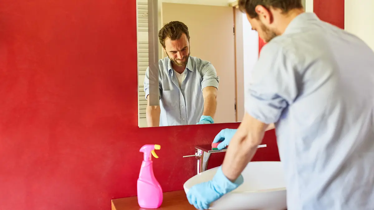 Hausmann beim Hausputz im Badezimmer putzt Waschbecken und Armatur