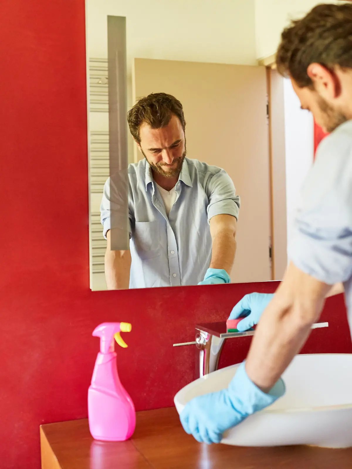Hausmann beim Hausputz im Badezimmer putzt Waschbecken und Armatur