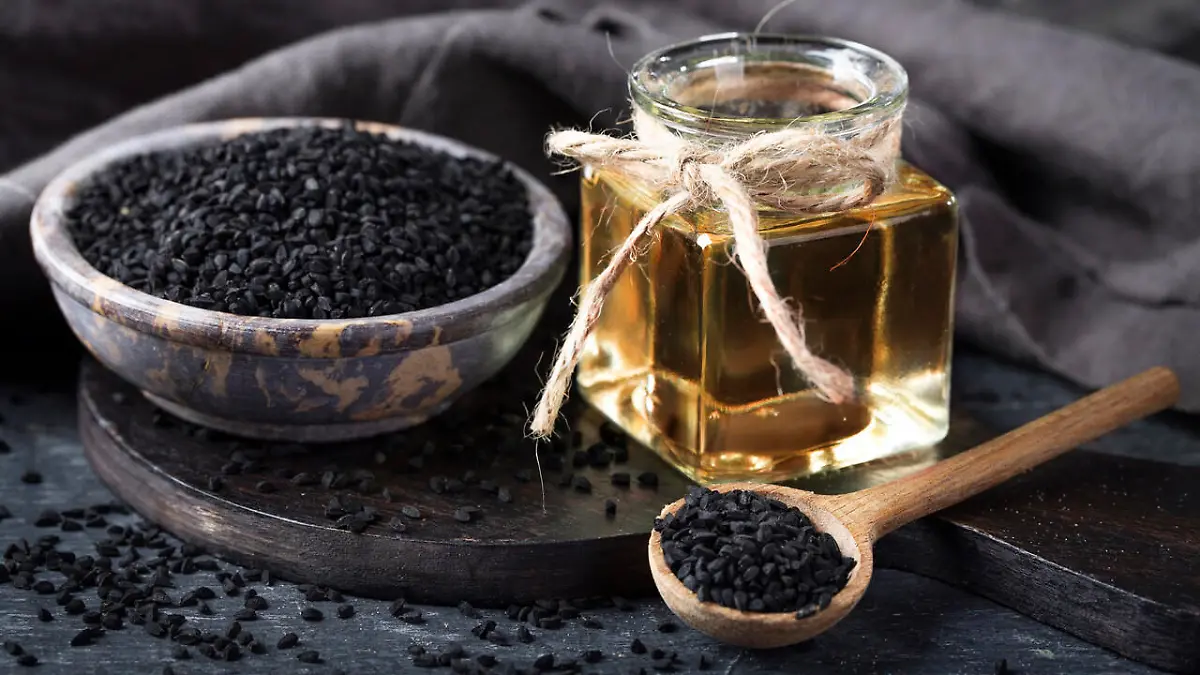 Black seeds in a bowl and oil on a black background