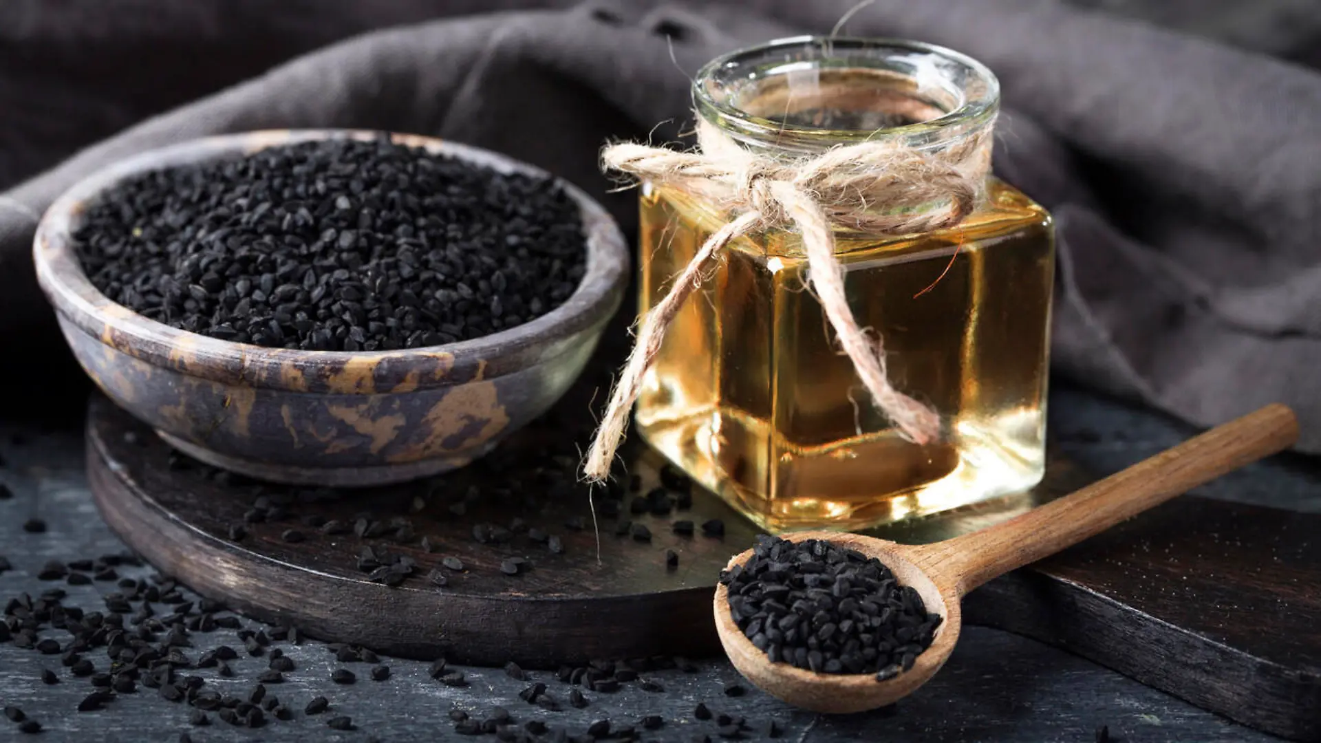 Black seeds in a bowl and oil on a black background