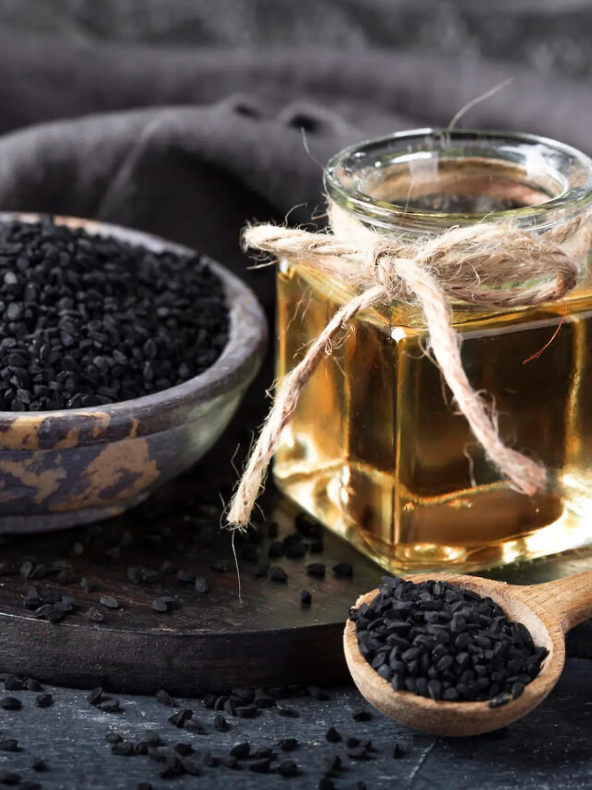 Black seeds in a bowl and oil on a black background