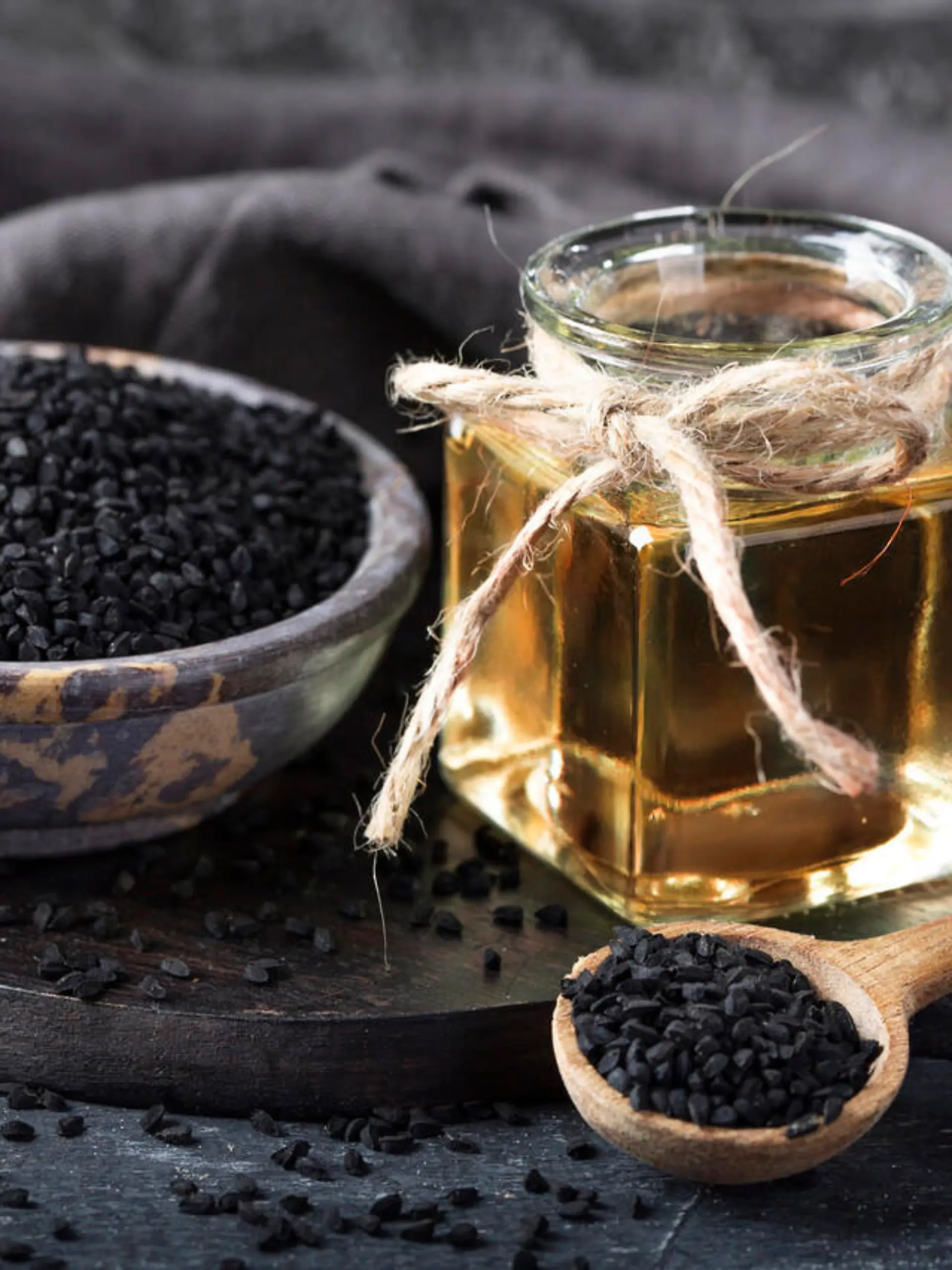 Black seeds in a bowl and oil on a black background