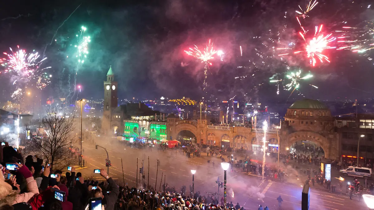 ARCHIV - 01.01.2020, Hamburg: Schaulustige beobachten um Mitternacht das Feuerwerk an den Hamburger Landungsbrücken. Rund um die Binnenalster und auf dem Rathausmarkt bleibt das Böllern in diesem Jahr verboten. (zu dpa: Feuerwerk rund um Binnenalster und auf Rathausmarkt verboten) Foto: Jonas Walzberg/dpa +++ dpa-Bildfunk +++