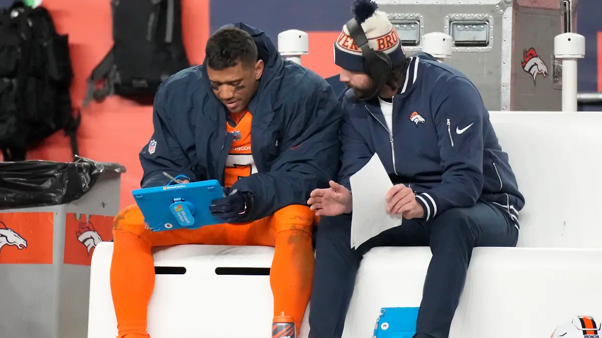 Denver Broncos quarterback Russell Wilson, left, looks over plays during the second half of an NFL football game against the New England Patriots, Sunday, Dec. 24, 2023, in Denver. (AP Photo/David Zalubowski)