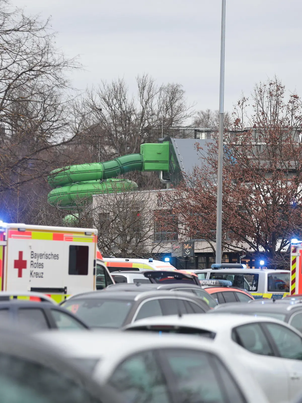 28.12.2023, Bayern, Neu-Ulm: Zahlreiche Einsatzkräfte stehen auf dem vollen Parkplatz eines Erlebnisbades in Neu-Ulm. Ein Junge im Grundschulalter wurde hier bei einem Unfall schwer bis lebensgefährlich verletzt. Foto: Ralf Zwiebler/dpa +++ dpa-Bildfunk +++