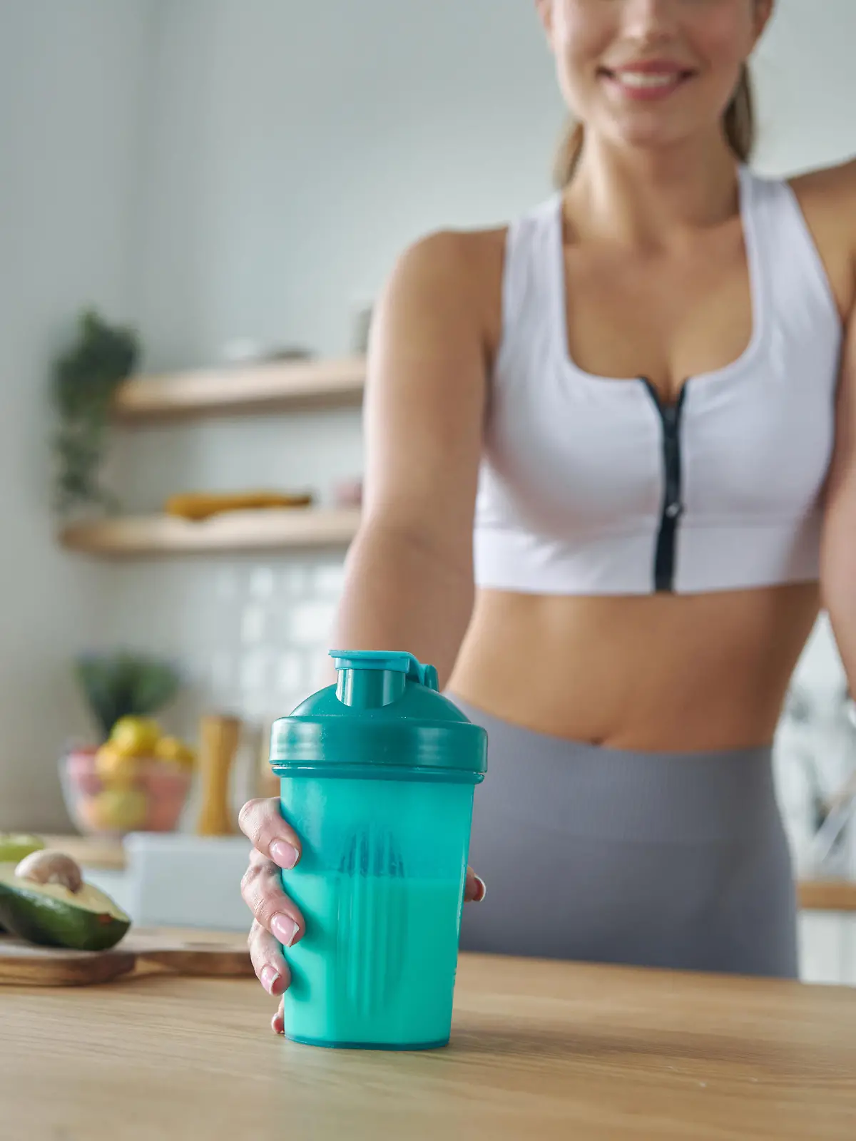 Close-up of woman in sports clothing holding shaker with protein cocktail at the kitchen