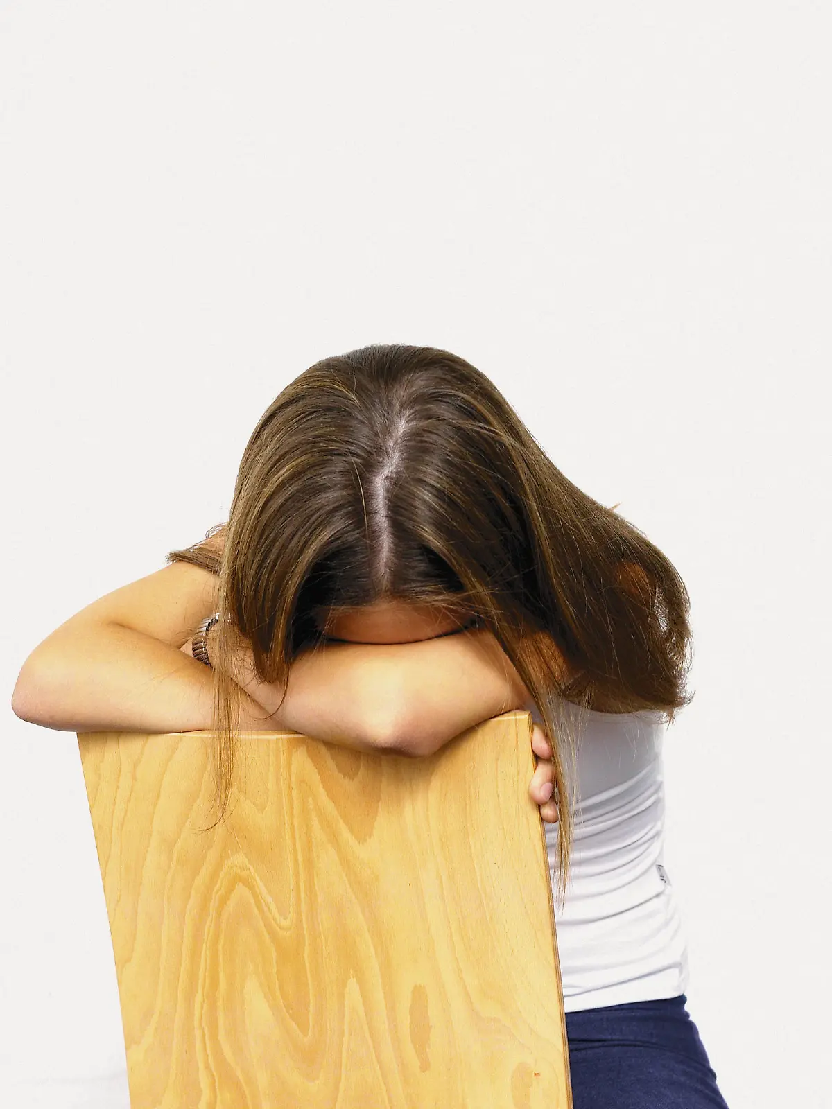 eine Teenagerin sitzt traurig, weinend auf dem Stuhl mit dem Kopf in Ihre Arme versunken stützend an die Stuhllehne.