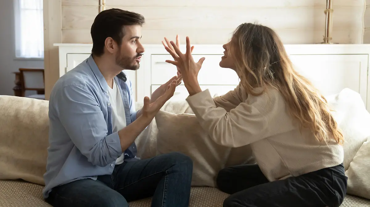 Emotional annoyed stressed couple sitting on couch, arguing at home. Angry irritated nervous woman man shouting at each other, figuring out relations, feeling outraged, relationship problems concept.