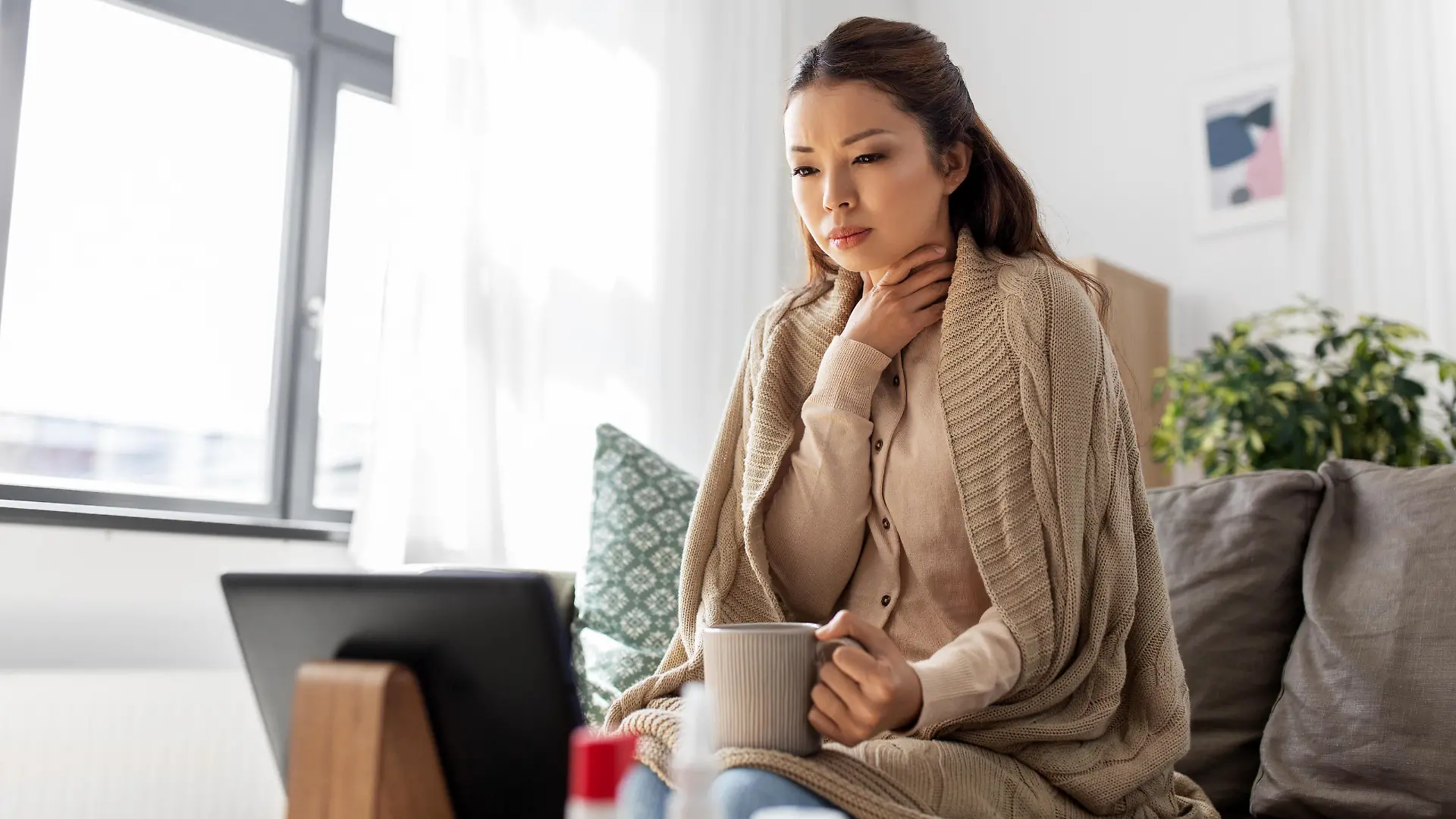 medicine, healthcare and technology concept - sick young asian woman having video call or online consultation on tablet pc computer and drinking tea at home