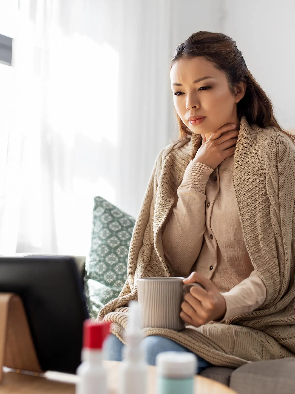 medicine, healthcare and technology concept - sick young asian woman having video call or online consultation on tablet pc computer and drinking tea at home