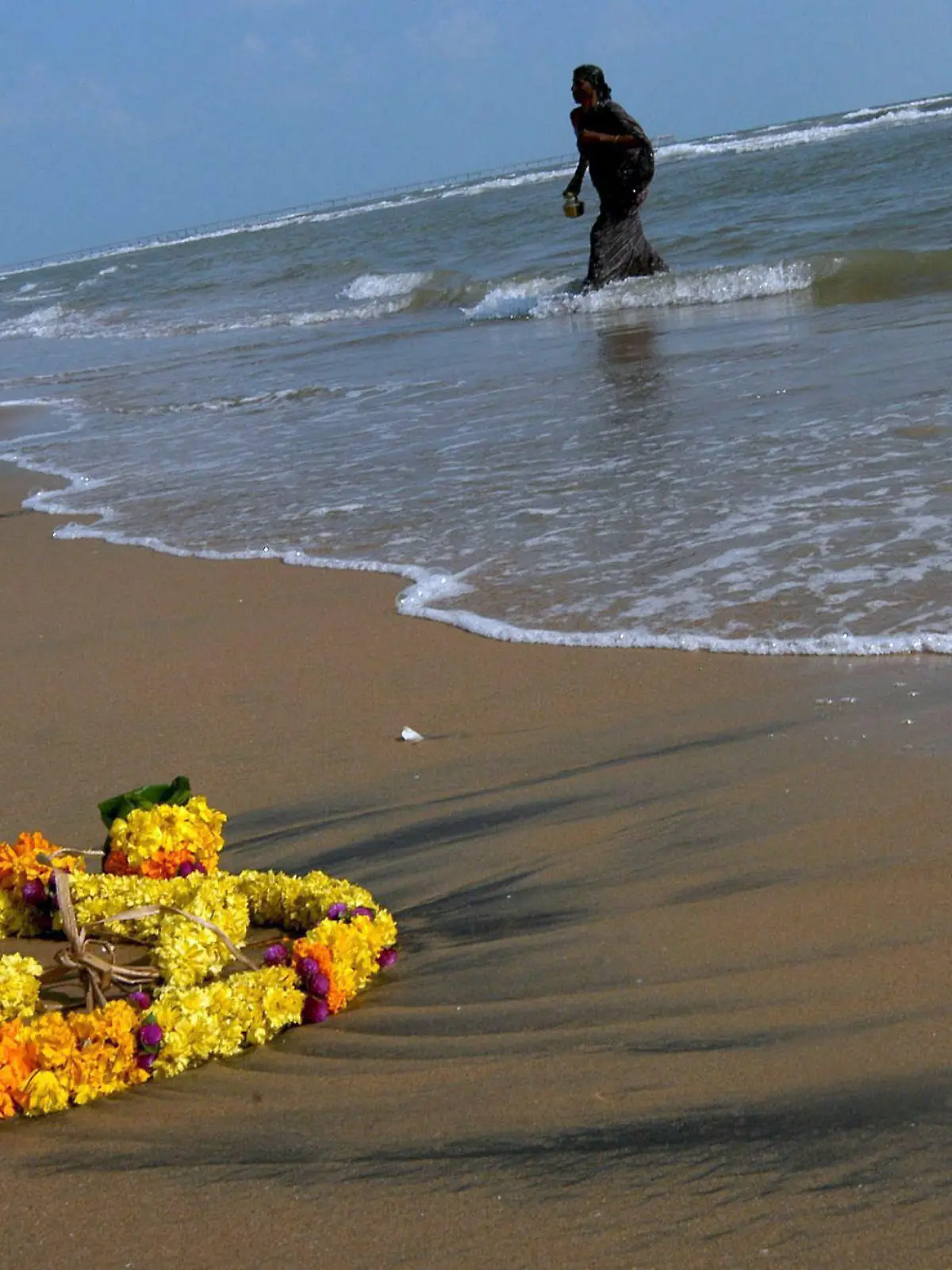 A flower garland used in a Hindu death ceremony for a Tsunami victim lies on the sandy beach after it was left into the sea along with other offerings by a family member (seen in the background), at the Samanthanpettai coast, Serathur village in Nagapattinam District in Tamil Nadu, India, on the early hours of Monday, 26 December 2005. Across India's southern coast and its Andaman and Nicobar islands, survivors of last year's tsunami remembered their dead on Monday with prayers, candlelight vigils and unveiling of memorials. EPA/MANJUNATH KIRAN +++(c) dpa - Bildfunk+++