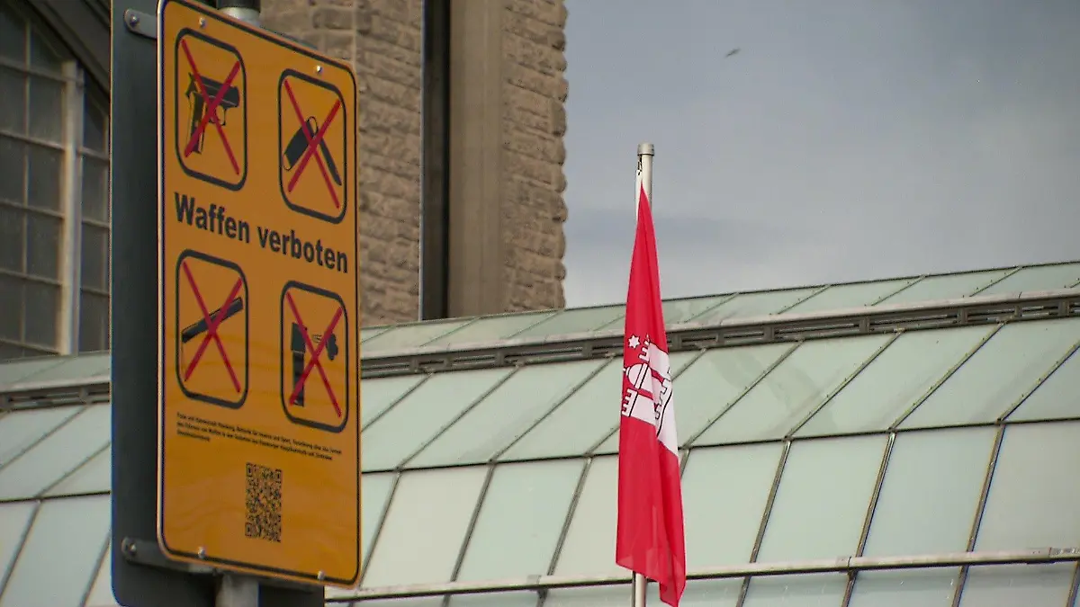 Ein Schild "Waffenverbotszone" am Hauptbahnhof neben einer hängenden Hamburg-Fahne.