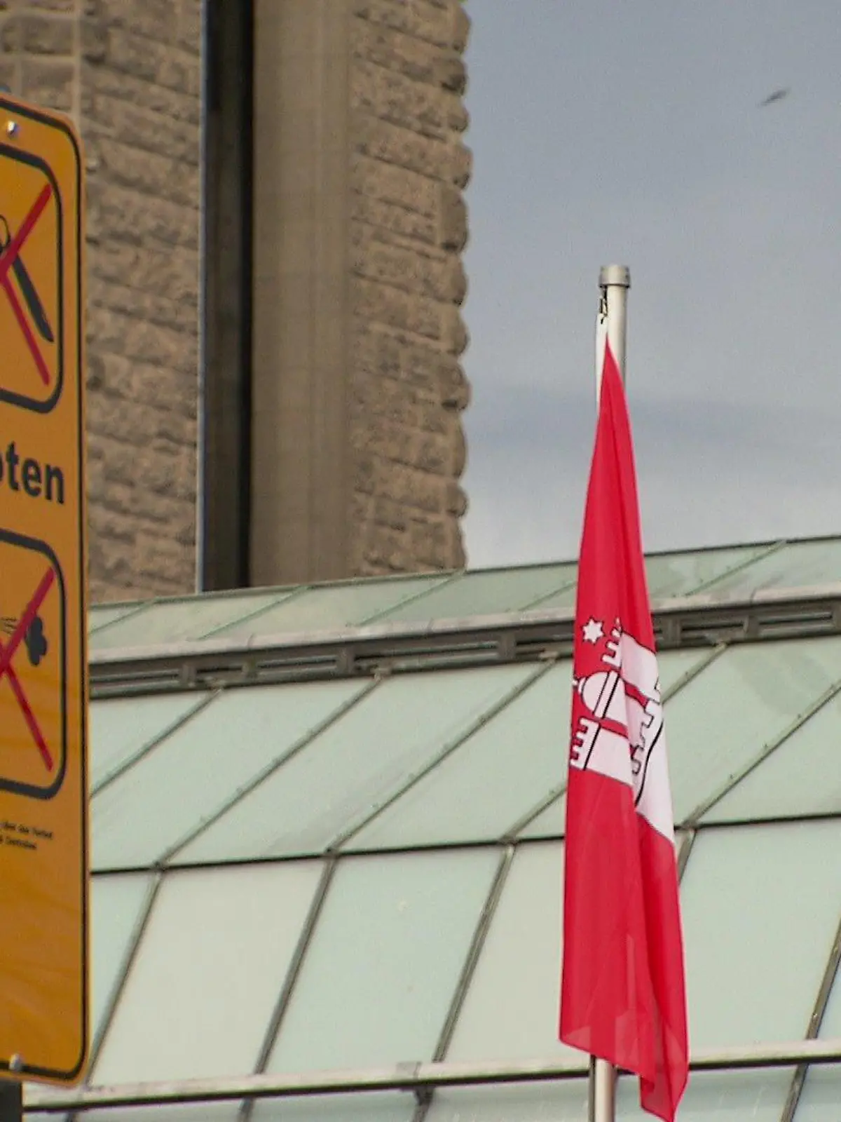 Ein Schild "Waffenverbotszone" am Hauptbahnhof neben einer hängenden Hamburg-Fahne.