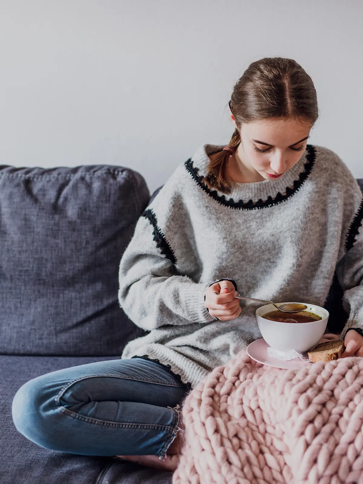 junge Frau sitz auf Sofa und isst Suppe (Foto: picture alliance / Mikelo / VisualEyze) || Modellfreigabe vorhanden
