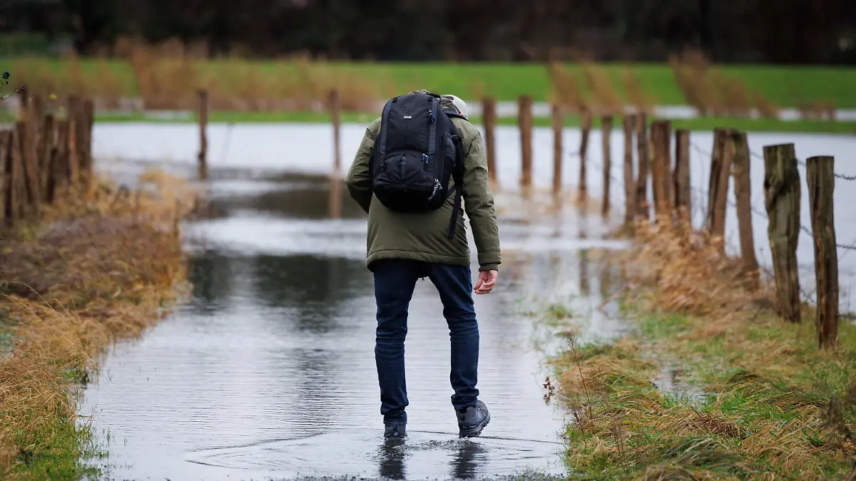 21.12.2023, Niedersachsen, Osnabrück: Ein Spaziergänger geht über den vom Regen überfluteten Teil eines Gehweges. Der Deutsche Wetterdienst rechnet insbesondere an der Nordseeküste mit Sturm, teils auch mit orkanartigen Böen. Außerdem besteht laut Experten die Gefahr von Sturmfluten. Foto: Friso Gentsch/dpa +++ dpa-Bildfunk +++