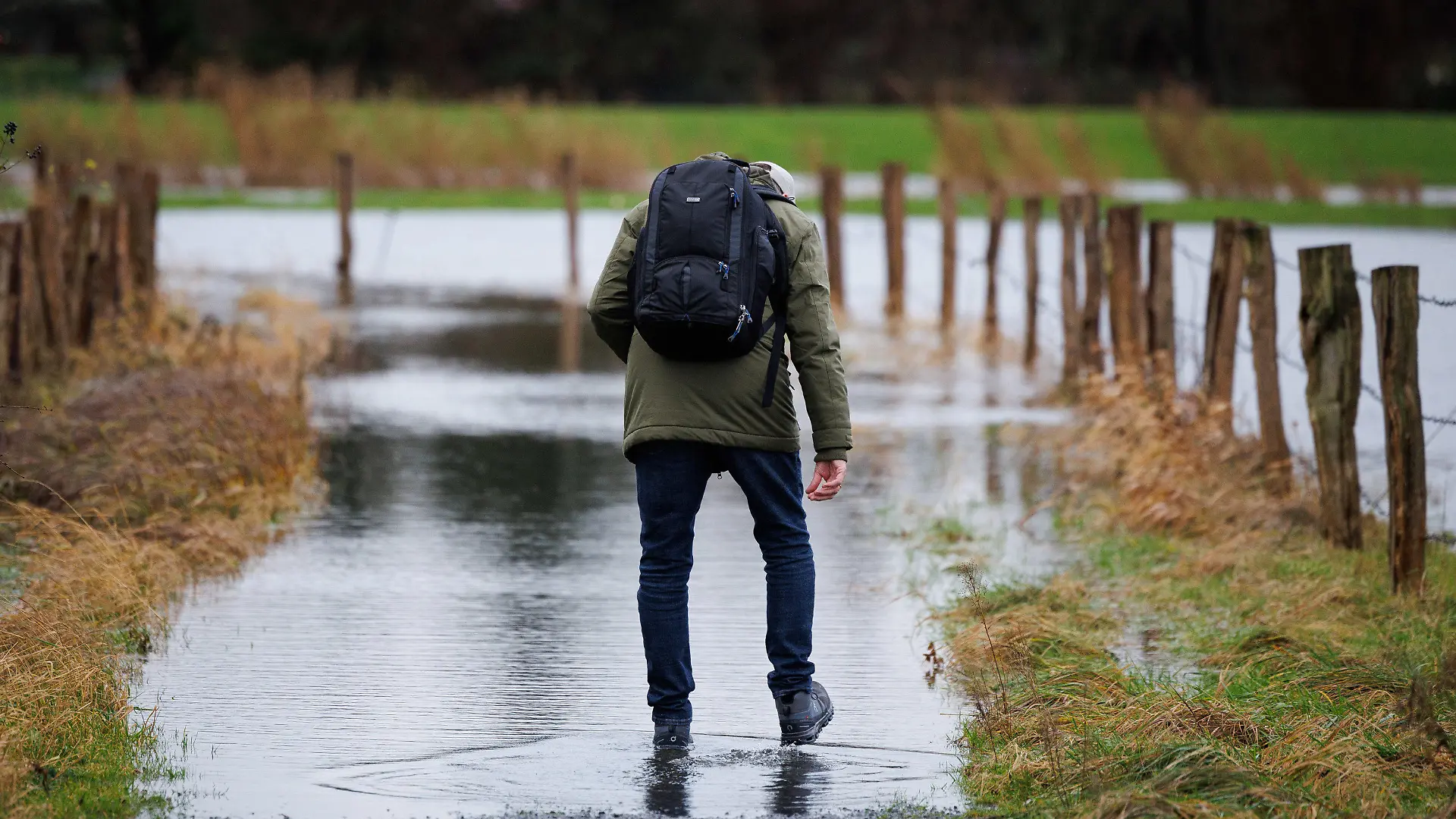 21.12.2023, Niedersachsen, Osnabrück: Ein Spaziergänger geht über den vom Regen überfluteten Teil eines Gehweges. Der Deutsche Wetterdienst rechnet insbesondere an der Nordseeküste mit Sturm, teils auch mit orkanartigen Böen. Außerdem besteht laut Experten die Gefahr von Sturmfluten. Foto: Friso Gentsch/dpa +++ dpa-Bildfunk +++