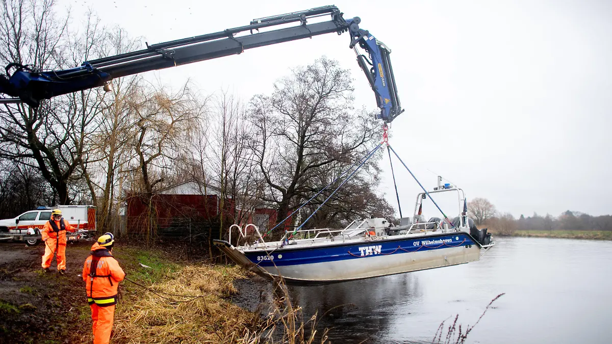 05.01.2024, Niedersachsen, Oldenburg: Einsatzkräfte der Technischen Hilfswerks (THW) heben mit einem Kran ein Boot aus der Hunte, mit dem sie zuvor treibende Baumstämme und Wurzeln aus dem Wasser entfernt haben. Die treibenden Stämme könnten den Deich und das nahegelegene Wasserkraftwerk an der Hunte beschädigen. Die Hochwasserlage an der Hunte bleibt angespannt. Foto: Hauke-Christian Dittrich/dpa +++ dpa-Bildfunk +++