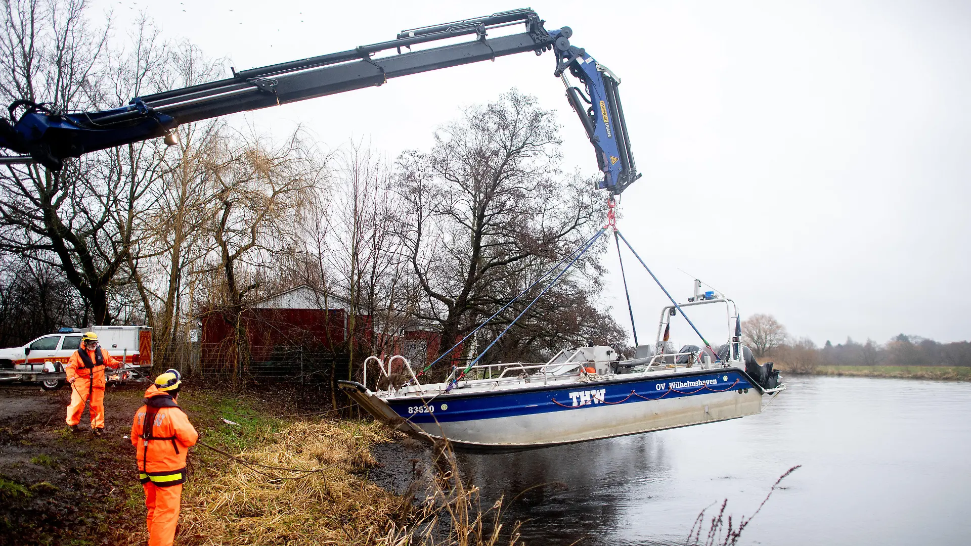 05.01.2024, Niedersachsen, Oldenburg: Einsatzkräfte der Technischen Hilfswerks (THW) heben mit einem Kran ein Boot aus der Hunte, mit dem sie zuvor treibende Baumstämme und Wurzeln aus dem Wasser entfernt haben. Die treibenden Stämme könnten den Deich und das nahegelegene Wasserkraftwerk an der Hunte beschädigen. Die Hochwasserlage an der Hunte bleibt angespannt. Foto: Hauke-Christian Dittrich/dpa +++ dpa-Bildfunk +++