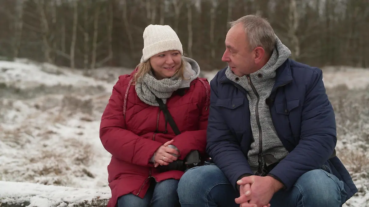 Die beiden Fotografen Karina und Timo Herzog sitzen auf einem Baumstamm. Beide lächeln und sehen einander an.
