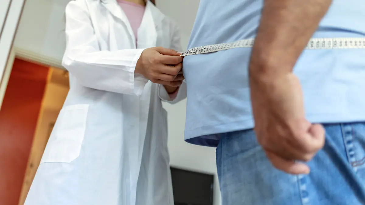 A nutritionist doctor measures the body of a male patient with a measuring tape on adipose tissue and excess weight. Overweight obesity man seeing doctor for treatment of his illness and weight loss.