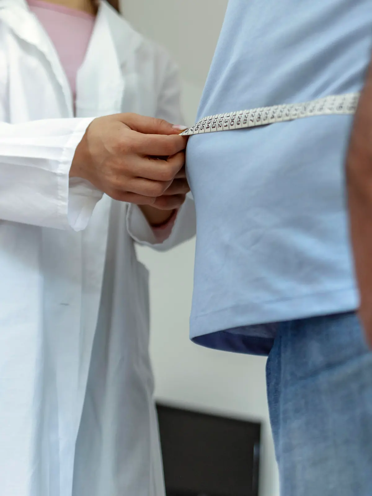 A nutritionist doctor measures the body of a male patient with a measuring tape on adipose tissue and excess weight. Overweight obesity man seeing doctor for treatment of his illness and weight loss.