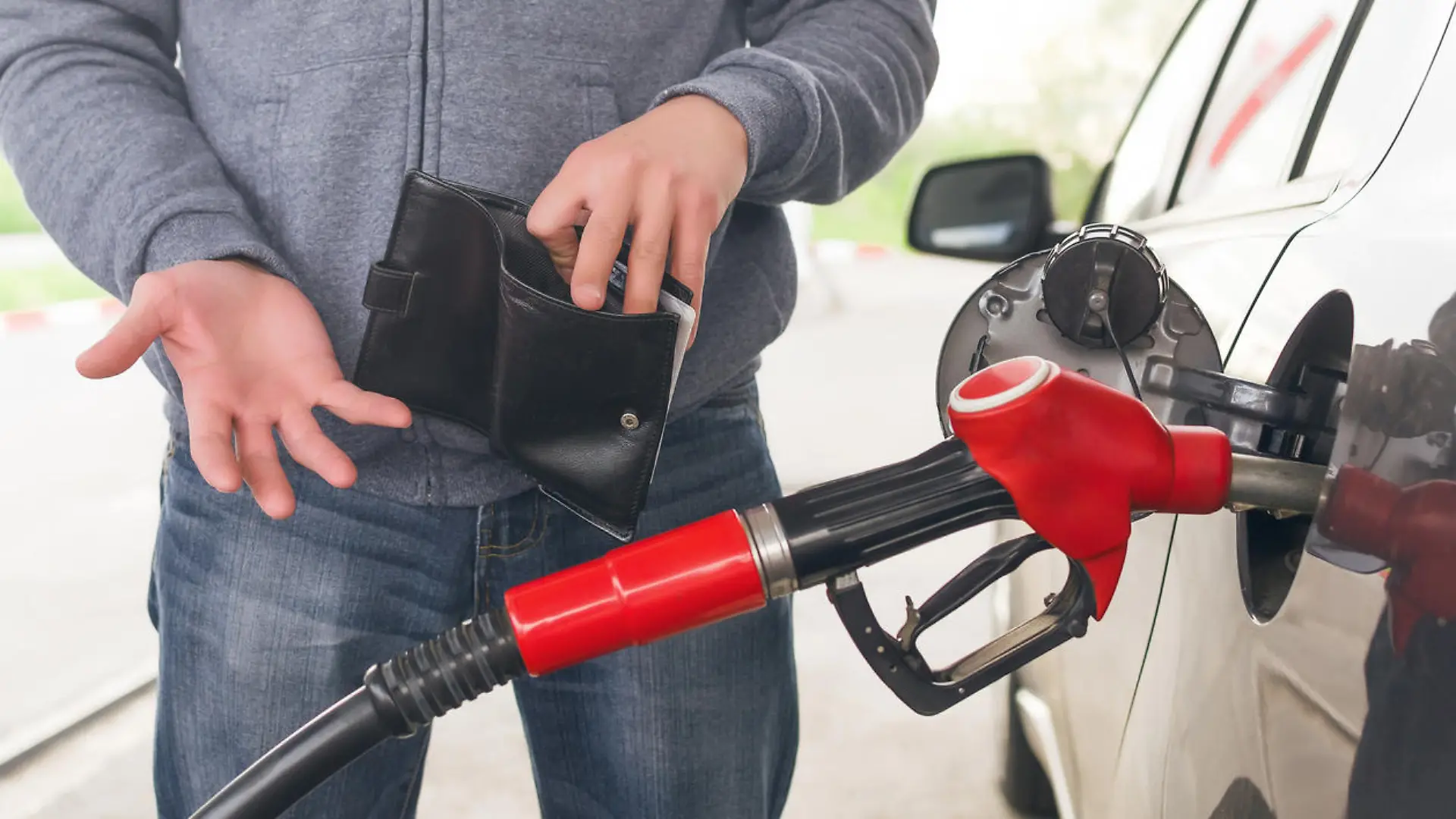 Lack of money for gasoline and fuel. Expensive gasoline. Driver man holds one dollar end empty wallet against the background of a fuel nozzle in the gas tank. increase in gasoline prices concept.