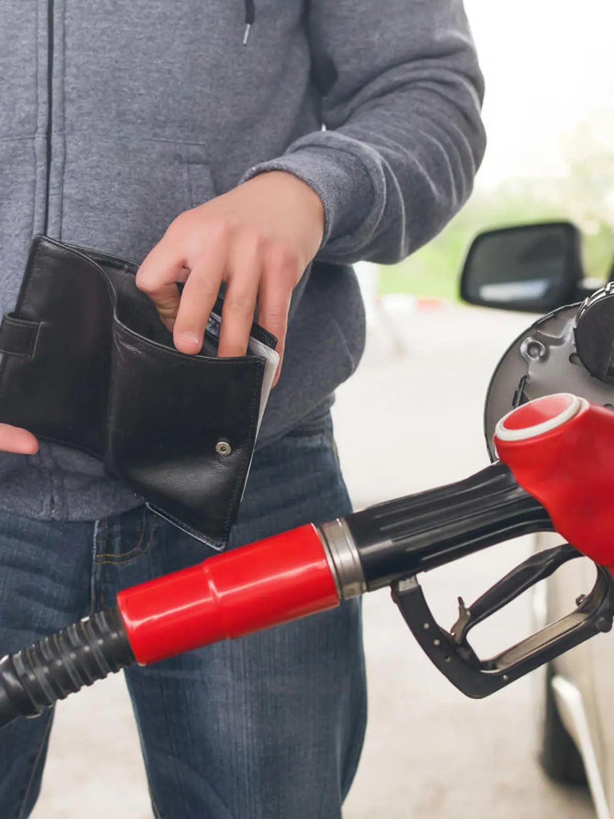 Lack of money for gasoline and fuel. Expensive gasoline. Driver man holds one dollar end empty wallet against the background of a fuel nozzle in the gas tank. increase in gasoline prices concept.