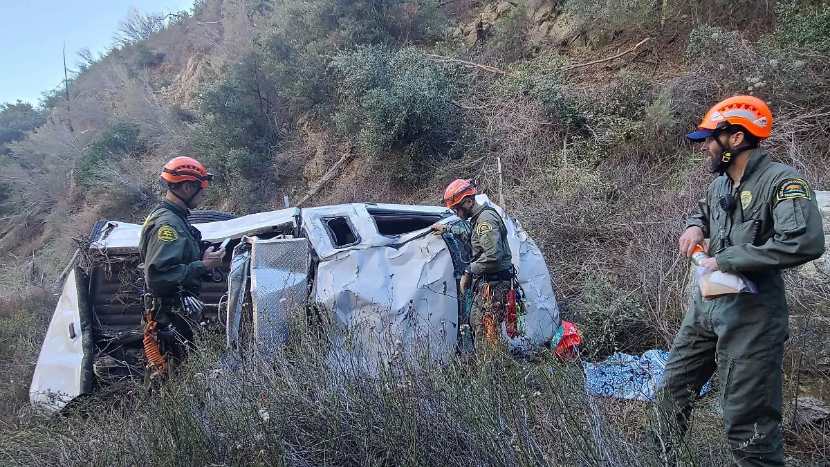 Ein Autowrack in einer Schlucht, daneben stehen Rettungskräfte.