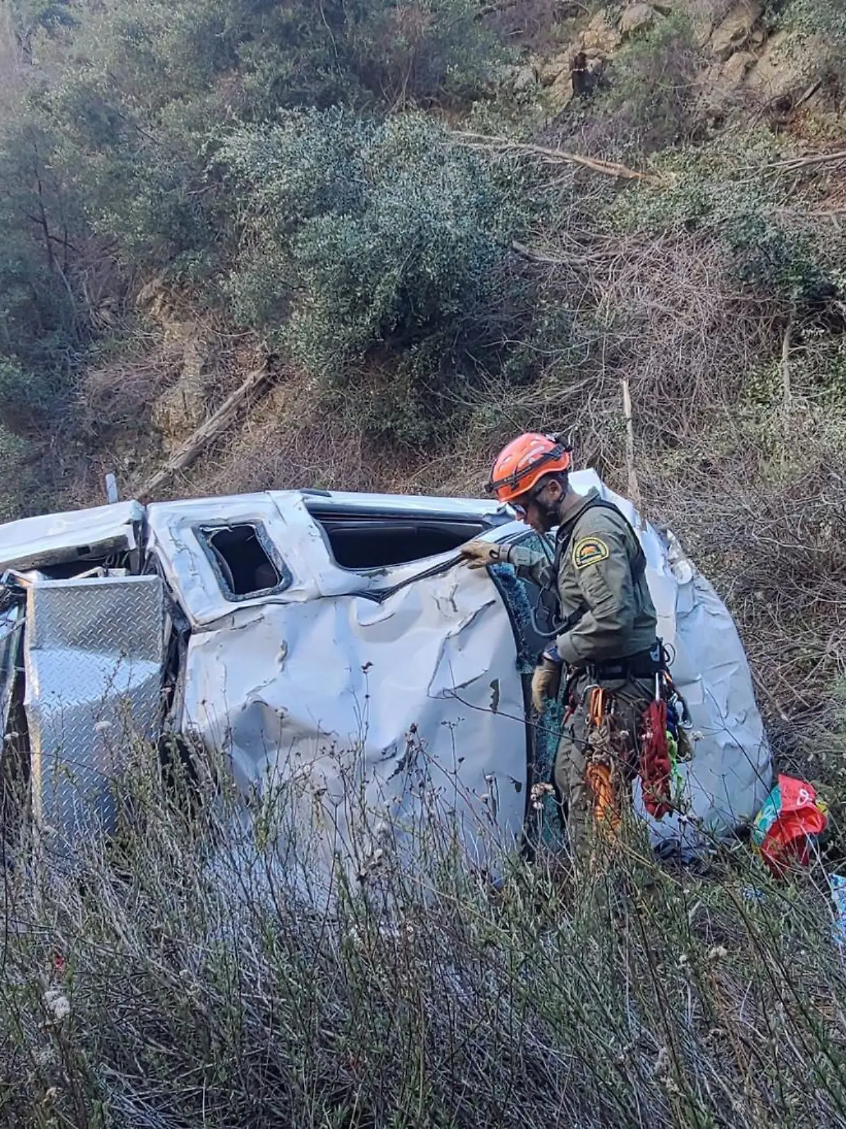 Ein Autowrack in einer Schlucht, daneben stehen Rettungskräfte.