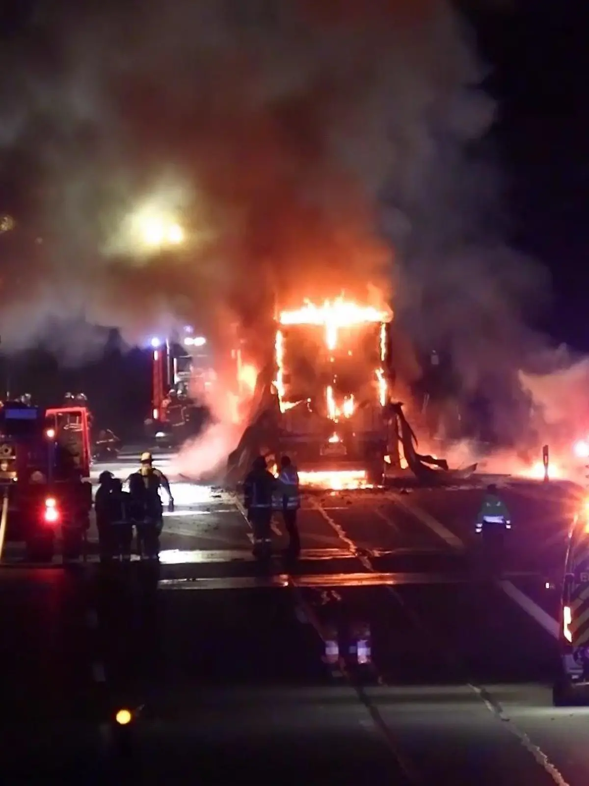 Ein brennender Lkw steht am rechten Rand einer dreispurigen Autobahn und brennt. Vier Feuerwehrfahrzeuge stehen um den brennenden Lkw herum, Feuerwehrkräfte versuchen den Brand zu löschen.