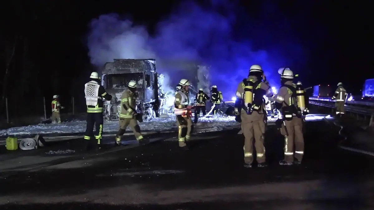 Feuerwehrkräfte stehen auf der Autobahn und löschen den brennenden Sattelzug mit Löschschaum.