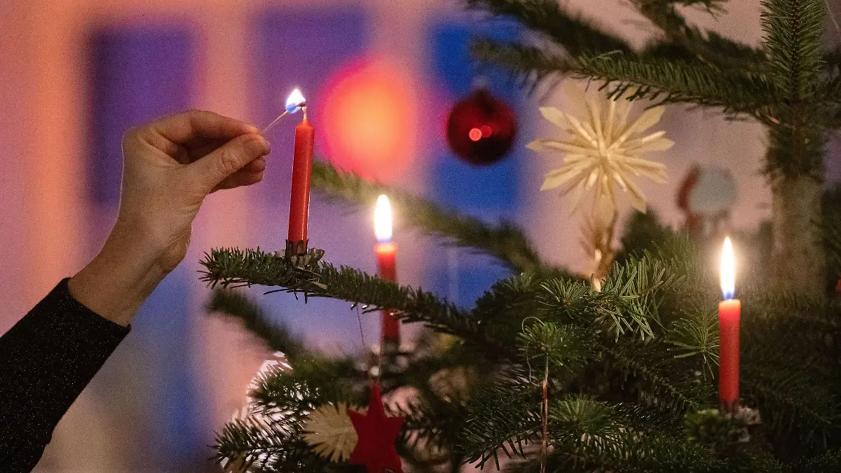 Eine Frau zündet eine Kerze an einem Weihnachtsbaum an.
