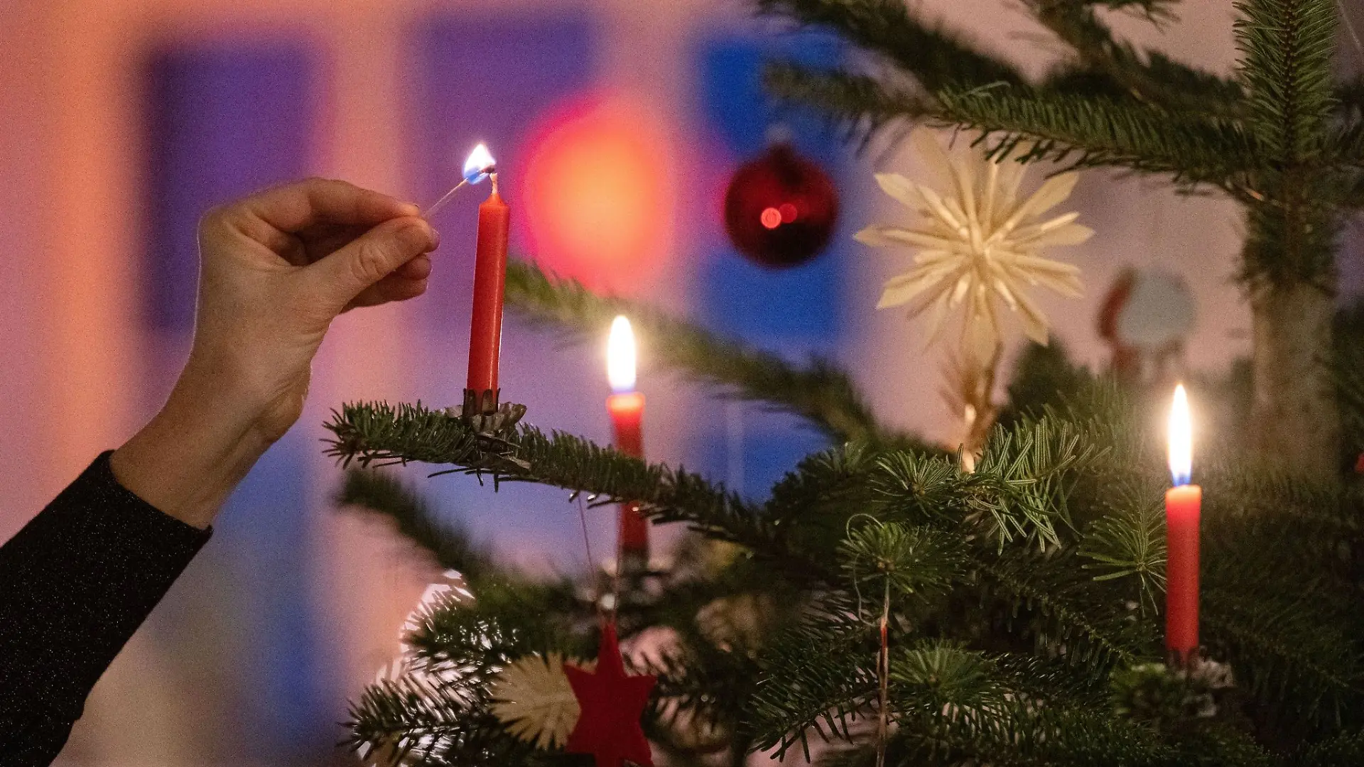 Eine Frau zündet eine Kerze an einem Weihnachtsbaum an.