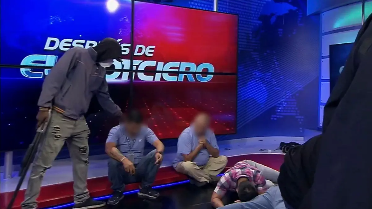 HANDOUT - 09.01.2024, Ecuador, Guayaquil: Dieser Screenshot eines Live-Videos des Fernsehsenders TC Television zeigt eine maskierte, bewaffnete Person, die sich während einer Live-Sendung über Journalisten stellt. In Ecuador sind Bewaffnete während einer Live-Übertragung in die Räumlichkeiten eines Fernsehsenders eingedrungen. Mehrere Journalisten und Mitarbeiter wurden von einer Gruppe von Kriminellen mit Maschinengewehren und Sprengstoff bedroht und als Geiseln genommen, wie am Dienstag auf Fernsehbildern zu sehen war. Foto: Uncredited/TC Television network/AP/dpa - ACHTUNG: Nur zur redaktionellen Verwendung bis zum 23.01.2024 und nur mit vollständiger Nennung des vorstehenden Credits +++ dpa-Bildfunk +++