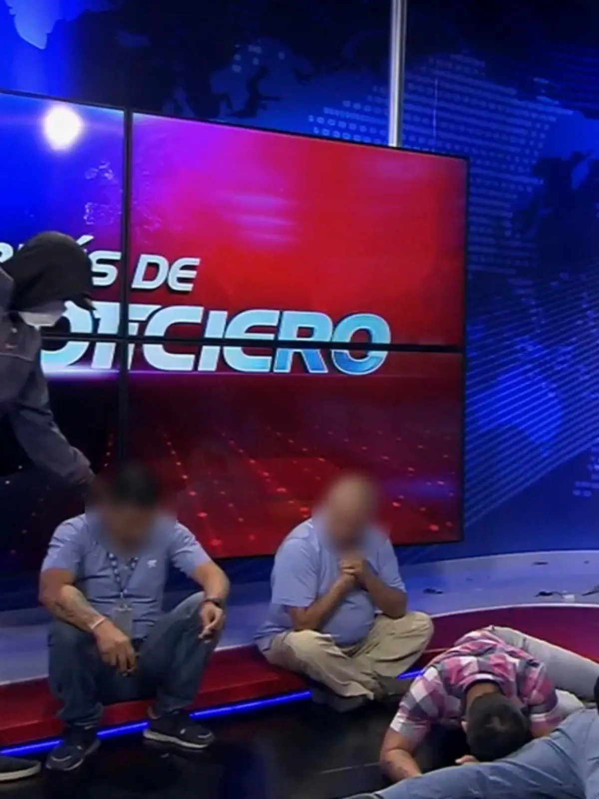 HANDOUT - 09.01.2024, Ecuador, Guayaquil: Dieser Screenshot eines Live-Videos des Fernsehsenders TC Television zeigt eine maskierte, bewaffnete Person, die sich während einer Live-Sendung über Journalisten stellt. In Ecuador sind Bewaffnete während einer Live-Übertragung in die Räumlichkeiten eines Fernsehsenders eingedrungen. Mehrere Journalisten und Mitarbeiter wurden von einer Gruppe von Kriminellen mit Maschinengewehren und Sprengstoff bedroht und als Geiseln genommen, wie am Dienstag auf Fernsehbildern zu sehen war. Foto: Uncredited/TC Television network/AP/dpa - ACHTUNG: Nur zur redaktionellen Verwendung bis zum 23.01.2024 und nur mit vollständiger Nennung des vorstehenden Credits +++ dpa-Bildfunk +++