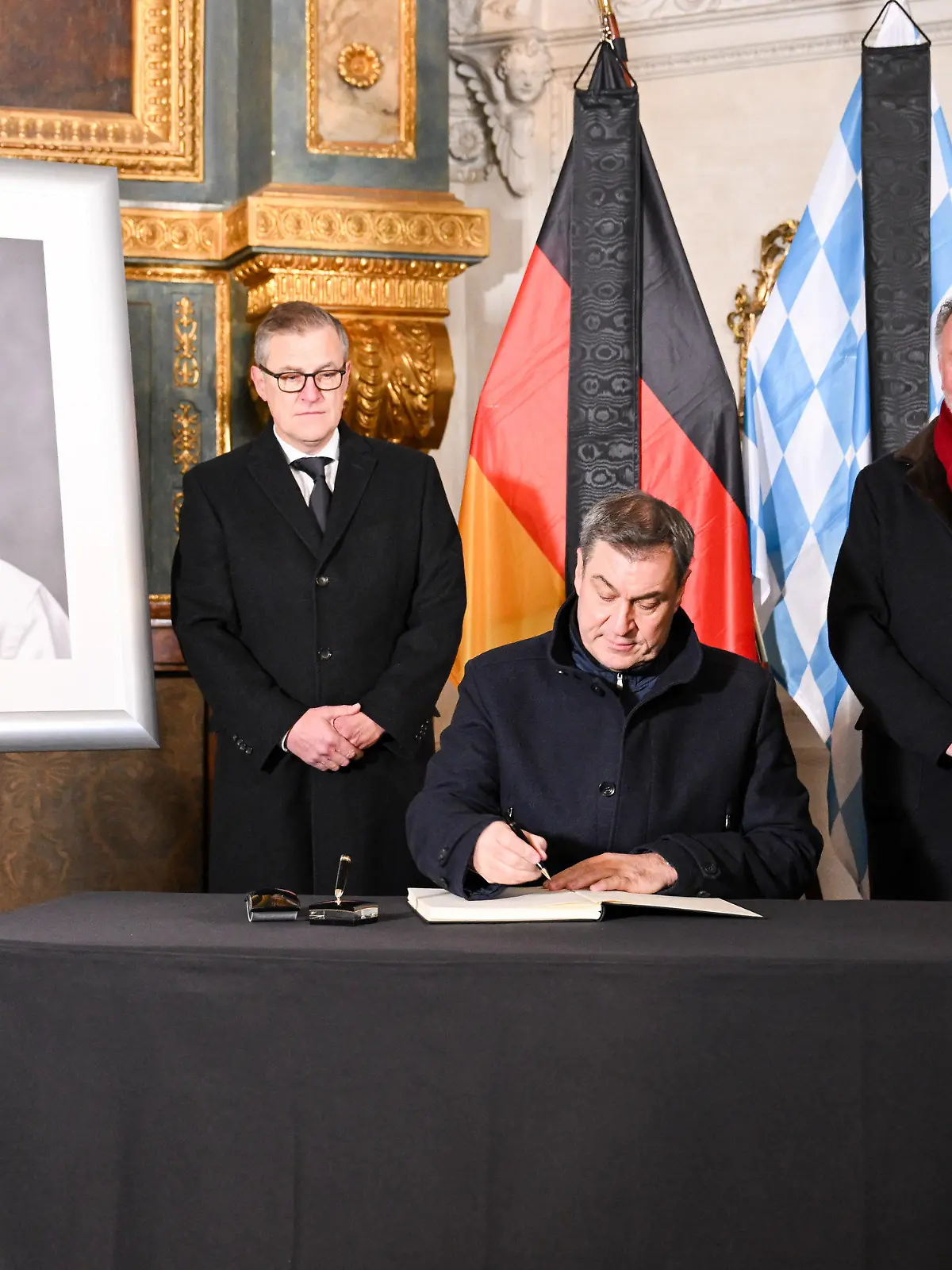 10.01.2024, Bayern, München: Fußball: Markus Söder (CSU), bayerischer Ministerpräsident, trägt sich in der Hofkapelle der Residenz in das Kondolenzbuch der bayerischen Staatsregierung in Trauer um Beckenbauer ein in Anwesenheit von Jan-Christian Dreesen (l-r), Vorstandsvorsitzender des FC Bayern, Karl-Heinz Rummenigge, Aufsichtsrat beim FC Bayern, und Herbert Hainer, Präsident des FC Bayern. Beckenbauer ist am Sonntag, 07.01.2024 im Alter von 78 Jahren gestorben. Foto: Tobias Hase/dpa - ACHTUNG: Nur zur redaktionellen Verwendung im Zusammenhang mit einer Berichterstattung über Beckenbauers Tod und nur mit vollständiger Nennung des vorstehenden Credits; nur volles Format, keine Ausschnitte; kein crop. +++ dpa-Bildfunk +++