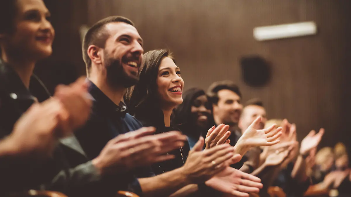 Group of smiling people clapping hands in the theater, close up of hands. Dark tone.