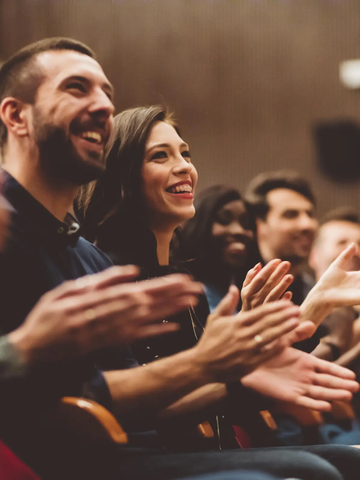 Group of smiling people clapping hands in the theater, close up of hands. Dark tone.