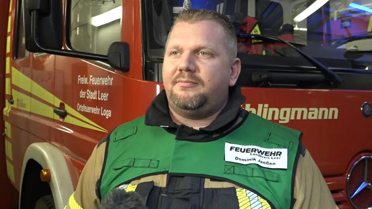 Ein Feuerwehrmann steht vor einem Feuerwehrauto und gibt ein Interview.