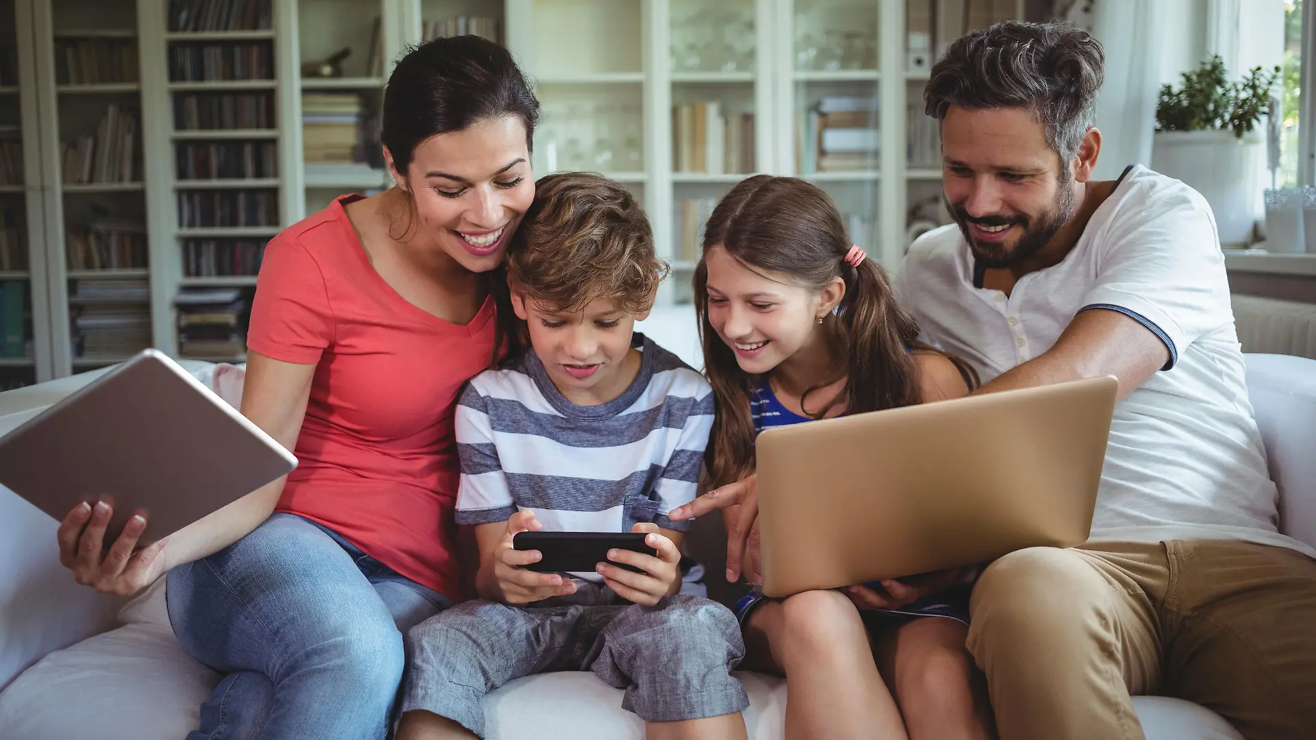 Happy family sitting on sofa and using laptop, mobile phone and digital tablet at home