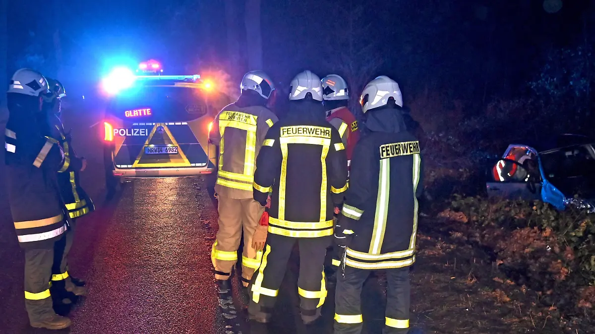 11.01.2024, Nordrhein-Westfalen, Dorsten: Im Einsatzfahrzeug der Polizei leuchtet auf einem Display der Hinweis «Glätte» an einer Unfallstelle. Einsatzkräfte der Feuerwehr stehen auf der Bundesstraße 58 an der Unfallstelle mit einem verunfallten Pkw, der witterungsbedingt von der glatten Fahrbahn in den Straßengraben geraten war. Foto: Foto Bludau/dpa +++ dpa-Bildfunk +++