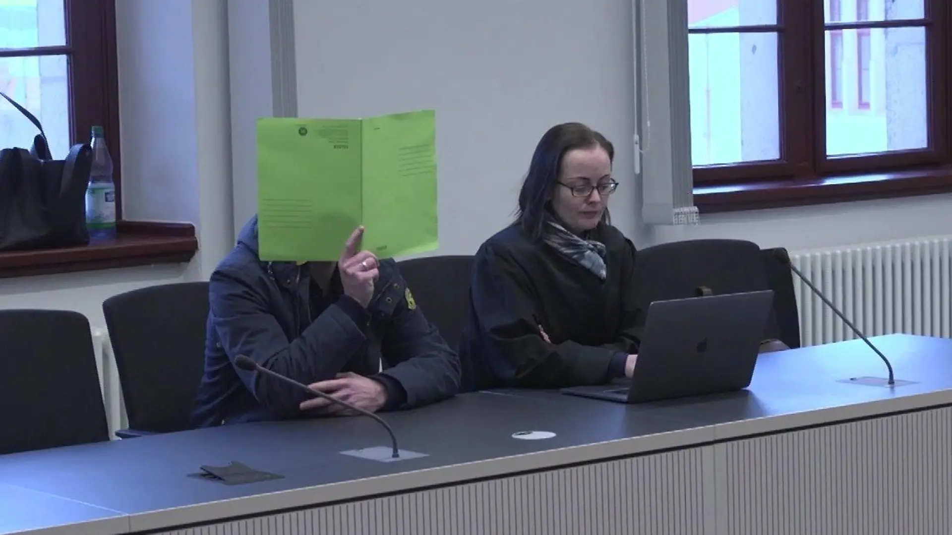 Versteckt hinter einer grünen Mappe betritt der Angeklagte den Saal des Landgerichts.