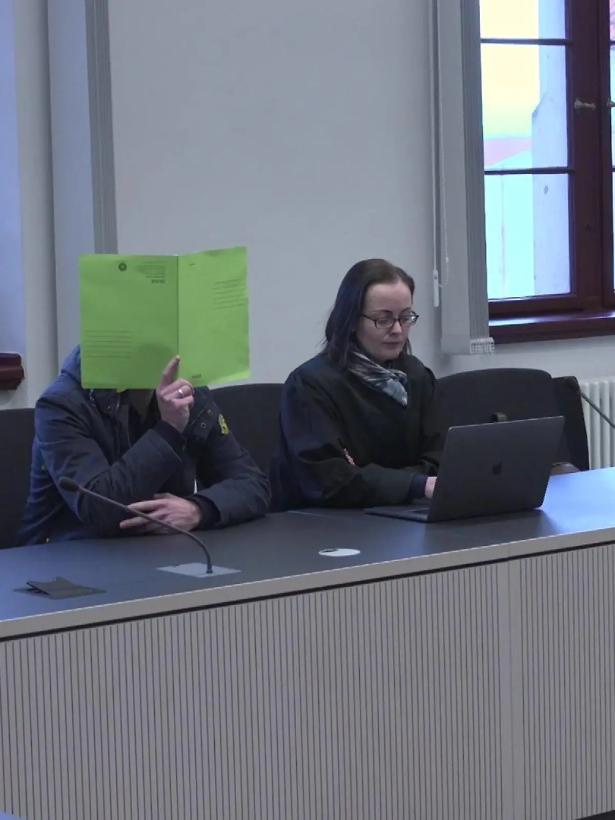 Versteckt hinter einer grünen Mappe betritt der Angeklagte den Saal des Landgerichts.