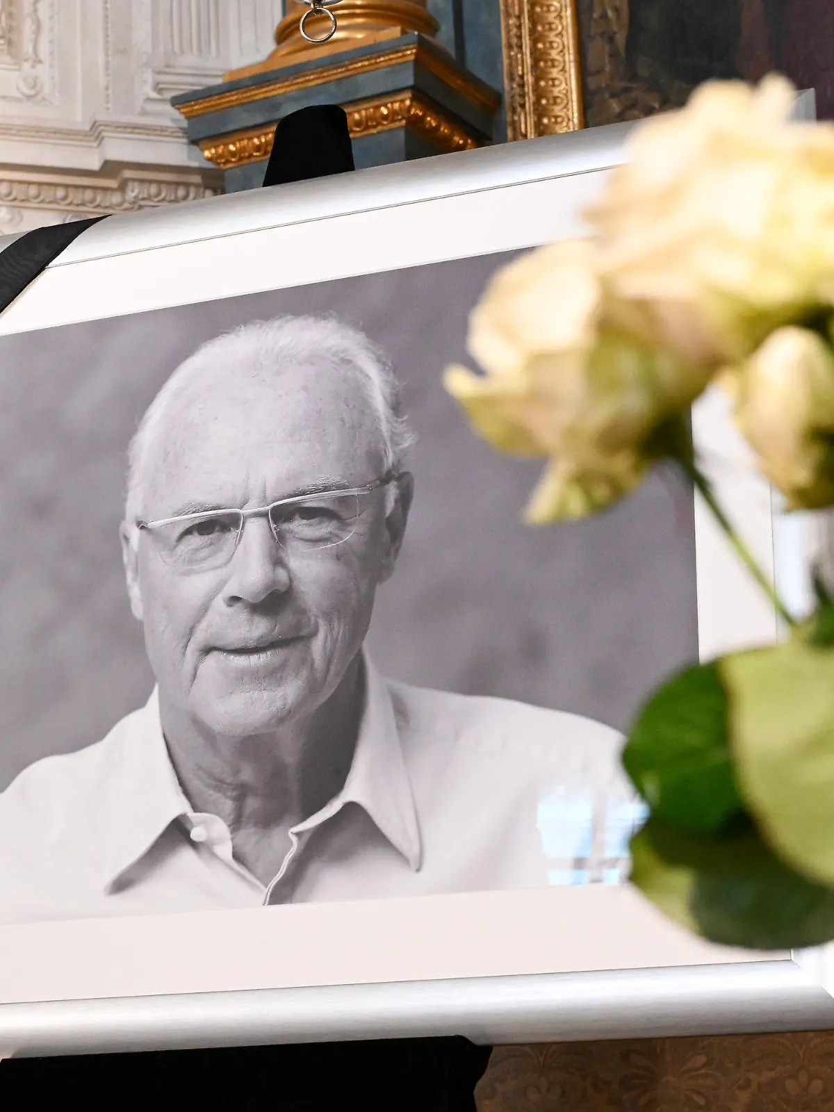 10.01.2024, Bayern, München: Fußball: Ein Porträt von Franz Beckenbauer ist neben einem Strauß weißer Rosen in der Hofkapelle der Residenz zu sehen. Beckenbauer ist am Sonntag, 07.01.2024 im Alter von 78 Jahren gestorben. Foto: Tobias Hase/dpa - ACHTUNG: Nur zur redaktionellen Verwendung im Zusammenhang mit einer Berichterstattung über den Tod von Beckenbauer und nur mit vollständiger Nennung des vorstehenden Credits; nur volles Format, keine Ausschnitte, kein crop +++ dpa-Bildfunk +++
