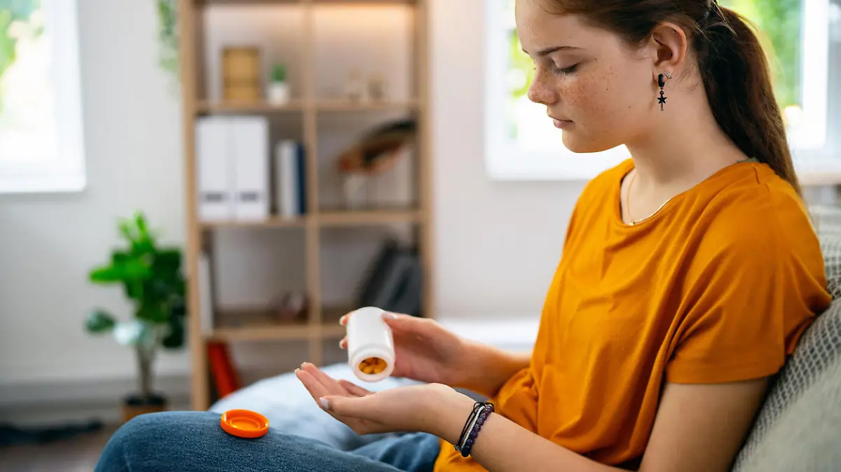 Caucasian redhead teenage girl, sitting on the sofa while taking pills