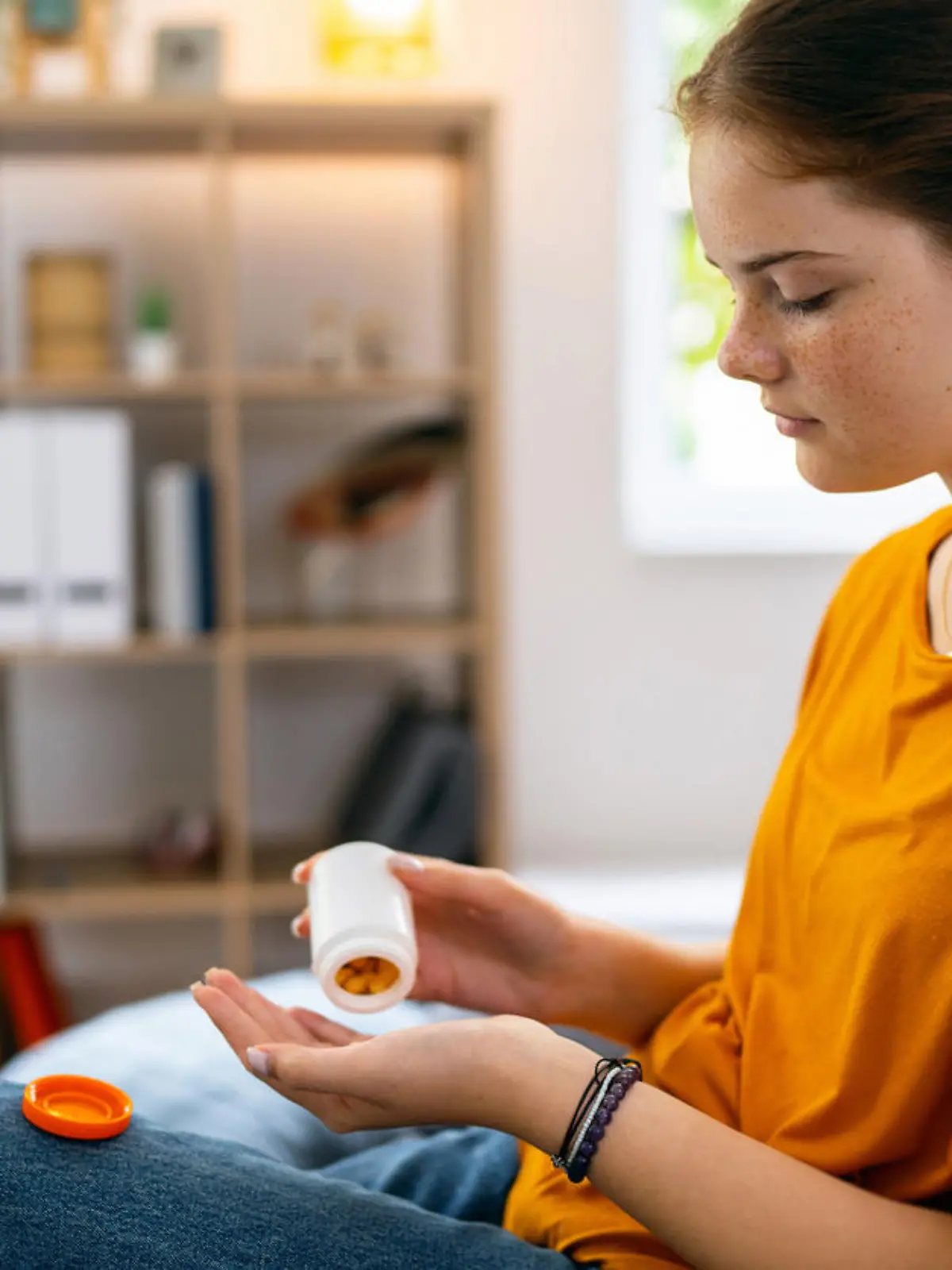 Caucasian redhead teenage girl, sitting on the sofa while taking pills