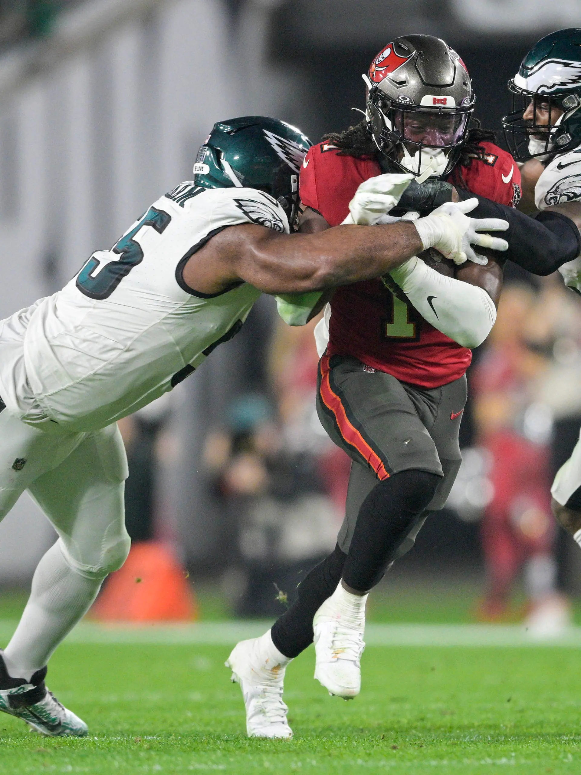 15.01.2024, USA, Tampa: American Football: Profiliga NFL, Play-off-Runde, Viertelfinal-Qualifikation, Tampa Bay Buccaneers - Philadelphia Eagles. Rachaad White (1), Running Back der Tampa Bay Buccaneers, in Aktion gegen Philadelphia Eagles Defensive End Brandon Graham (55) und Linebacker Zach Cunningham (52). Foto: Phelan M. Ebenhack/AP/dpa +++ dpa-Bildfunk +++