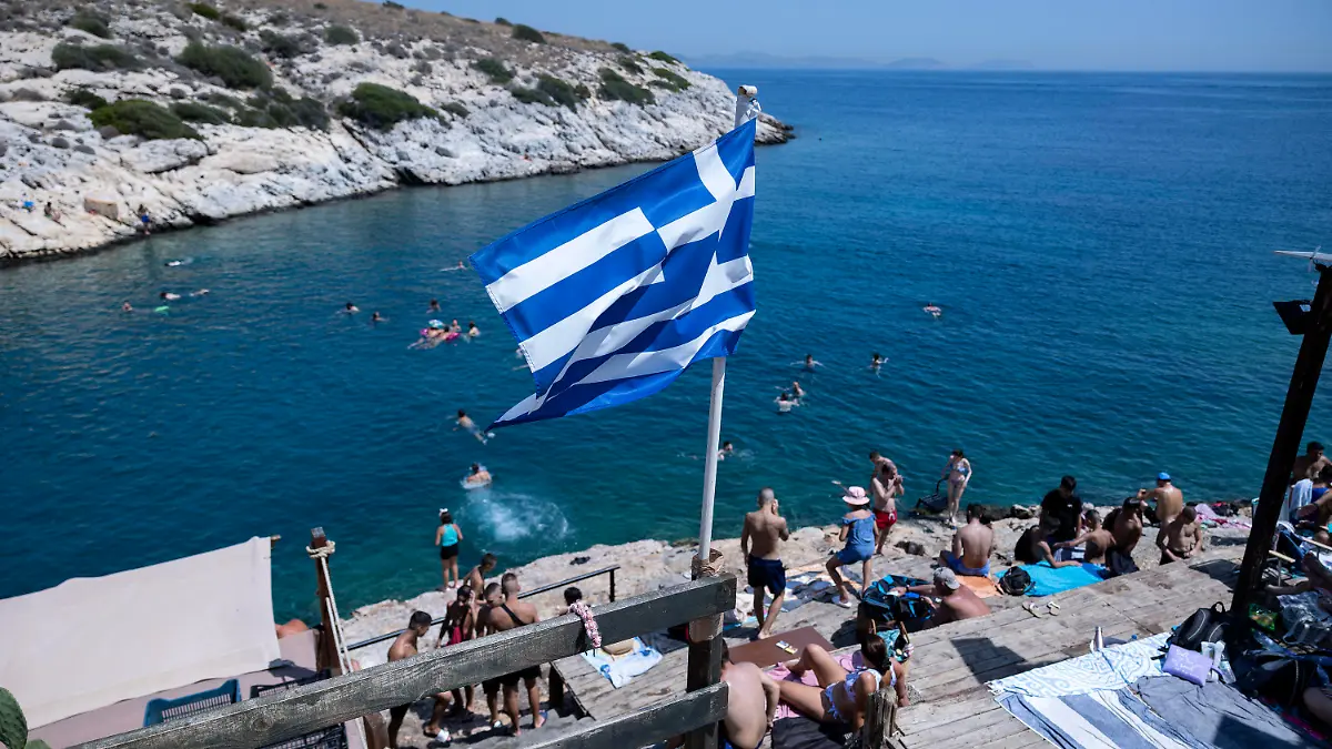 22.07.2023, Griechenland, Athen: Schwimmer sitzen auf Felsen am Meer im Vorort Vioulagmeni, südöstlich von Athen. Es wird erwartet, dass sich die Hitze in Griechenland im Laufe des Wochenendes verstärkt und sich 44 Grad Celsius nähert. Das ganze Land soll bis Ende Juli eine weitere Hitzewelle erleben. Foto: Yorgos Karahalis/AP/dpa/dpa +++ dpa-Bildfunk +++