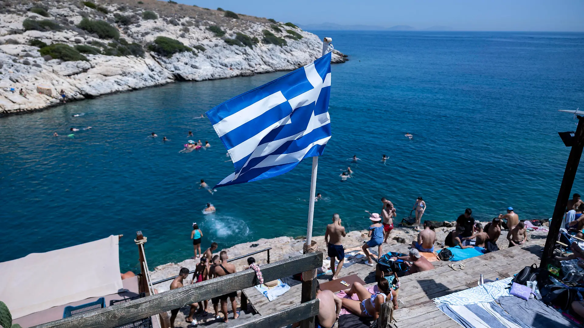 22.07.2023, Griechenland, Athen: Schwimmer sitzen auf Felsen am Meer im Vorort Vioulagmeni, südöstlich von Athen. Es wird erwartet, dass sich die Hitze in Griechenland im Laufe des Wochenendes verstärkt und sich 44 Grad Celsius nähert. Das ganze Land soll bis Ende Juli eine weitere Hitzewelle erleben. Foto: Yorgos Karahalis/AP/dpa/dpa +++ dpa-Bildfunk +++